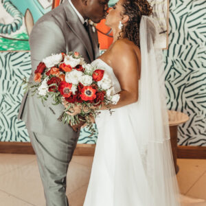 A bride and groom share a kiss with her beautiful bouquet by Render Events front and center.